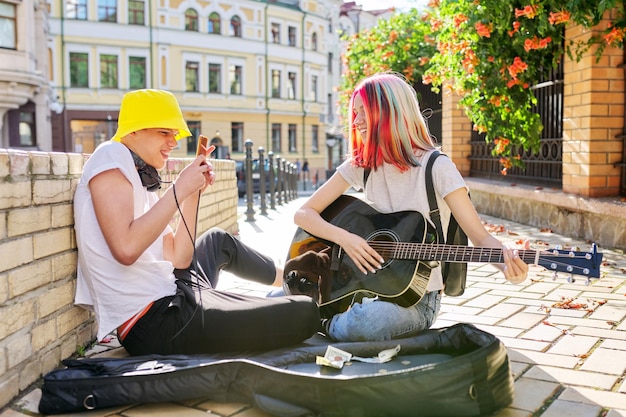 Couple of teenage hipsters street musicians making money by\
music