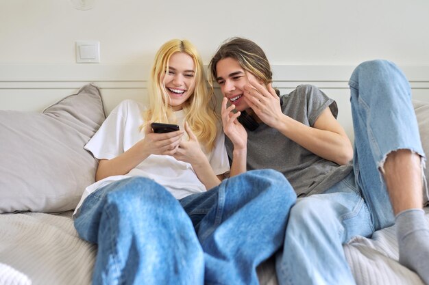 Couple of teenagers having fun together sitting on the couch looking into the smartphone