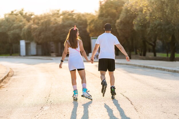 Couple in their backs skating while holding hands in an urban park