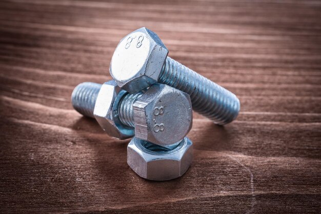 Couple of threaded metal bolts and screw nuts on vintage wooden board repairing concept