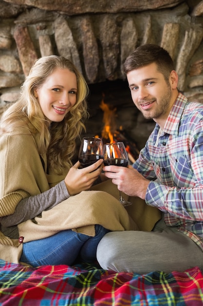 Couple toasting wineglasses in front of lit fireplace