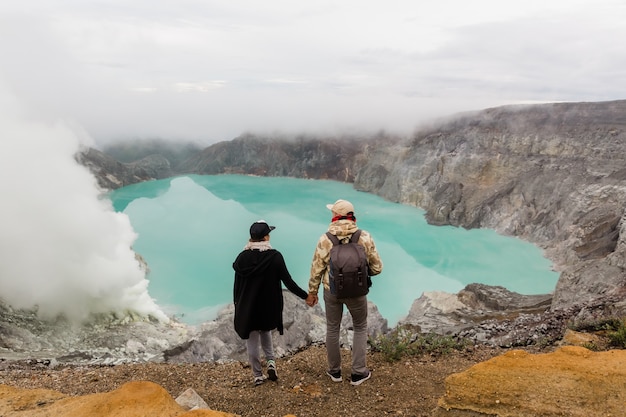 カップルの観光客は、インドネシアのジャワ島のイジェン火山の硫黄湖を見ています。ハイカーはトップマウンテン、旅行の概念に旅行します。