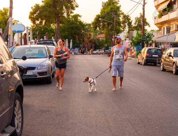 A couple tourists man and woman walk a Jack Russell Terrier dog on the embankment in Greece