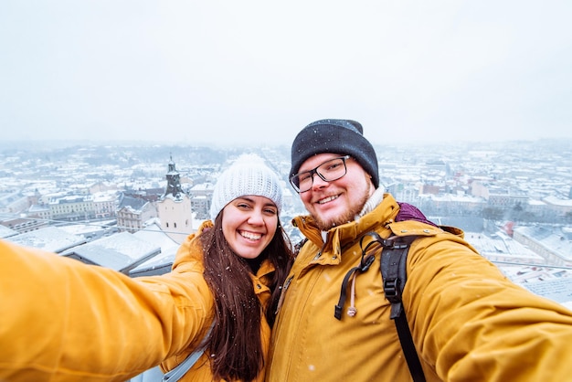 バック グラウンドで冬時間の美しい街の景色と selfie を取っているカップルの観光客