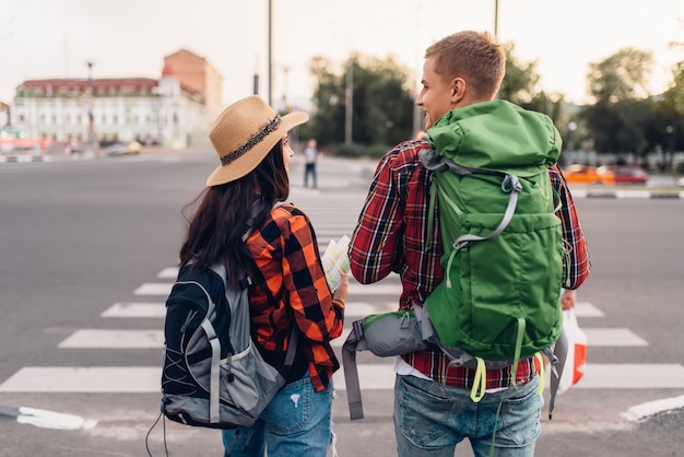 Couple of tourists with backpacks, back view, excursion in town. Summer hiking. Hike adventure of young man and woman, city walking