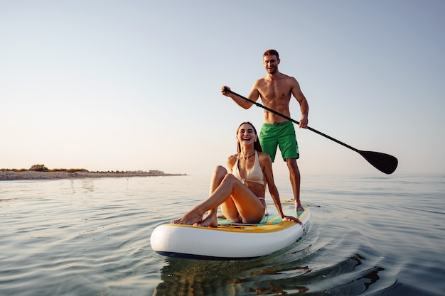 照片的游客的年轻男人和女人玩海上paddleboarding