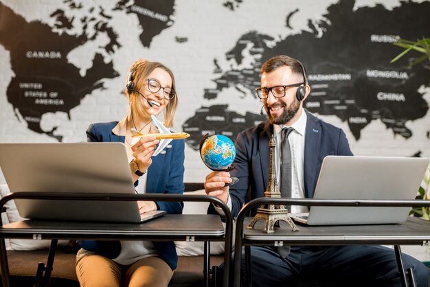 Photo couple of travel managers playing with globe and airplane sitting at the agency office with world map on the background