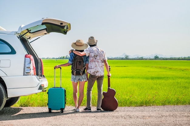 旅行者のカップルは、荷物とギターが車の近くに立っています。