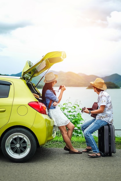 Couple of traveler sitting on hatchback car and play guitar