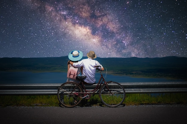 Photo couple traveler sitting near a bicycle and looking for the milky way and stars on the sky