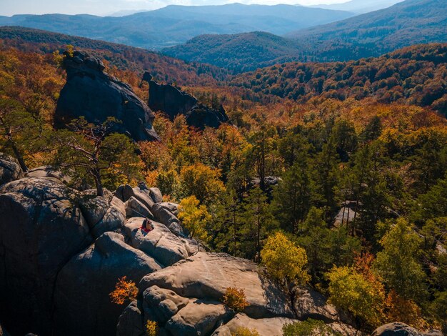 Couple traveler sitting on the top of the rock with beautiful landscape of autumn forest