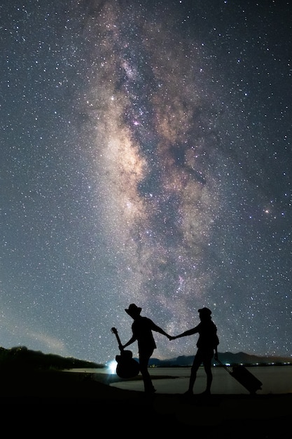 写真 湖の近くに立っていて、天の川と星空を見ているカップルの旅行者