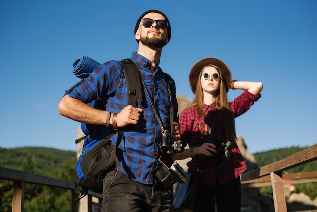 バックパック、ビンテージカメラ、双眼鏡で流行に敏感な服を着て山を旅するカップル