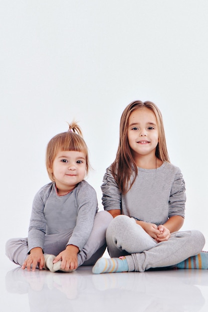 Couple of twins sitting on the floor isolated on a white background children in gray clothes