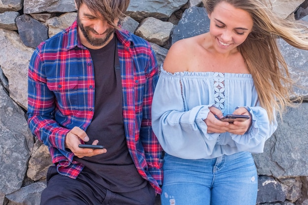 Couple of two adults using their phones together outdoors - technology concept and online lifestyle - beautiful woman and handsome man having fun together