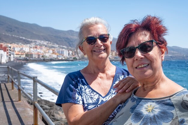 Couple of two female friends enjoying sea excursion  leaning against the railing of the seafront in a sunny day - wind, waves and seascape in Tenerife