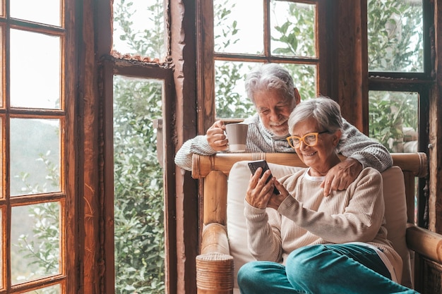 Пара двух пожилых и зрелых людей дома вместе пользуются телефоном на диване. Старшие используют смартфон, развлекаясь и наслаждаясь его просмотром.