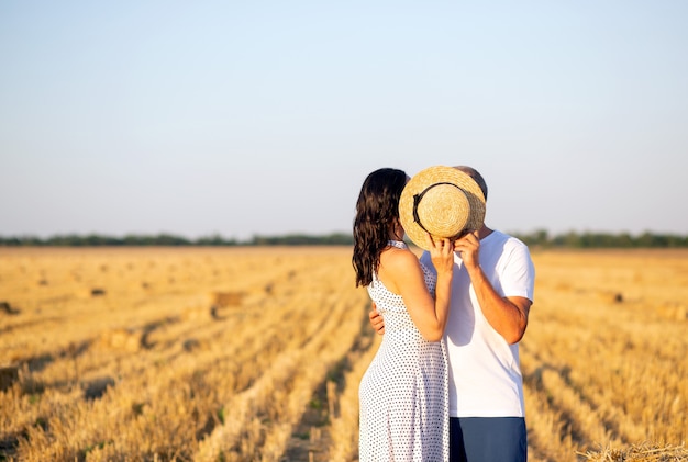 a couple of two people in love are standing on the field, kissing behind a straw hat