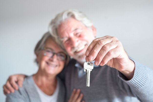 Couple of two seniors after buy a new house or car and go to live together - man holding a key and mature man and woman looking at it