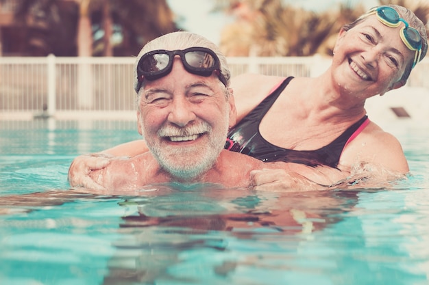 Coppia di due anziani abbracciati nell'acqua della piscina - uomo e donna attivi che fanno esercizio insieme in piscina - abbracciati con amore