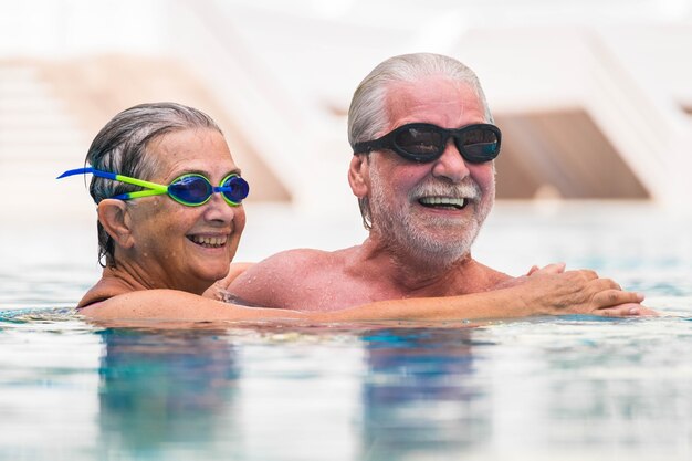 Couple of two seniors and mature people together in the pool swimming and having fun hugged - active and fitness lifestyle and concept