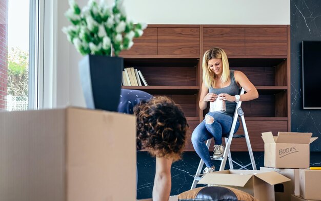 Photo couple unpacking moving boxes and placing things on the shelf