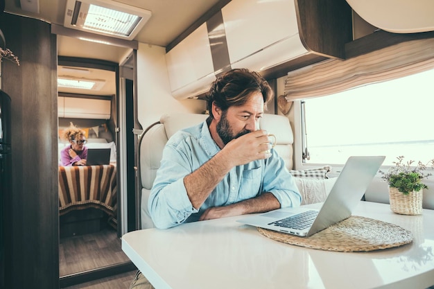 Couple use computer inside camper van during travel vacation or van life lifestyle Modern man and woman work together on laptop in alternative office motor home Digital nomad and smart free working