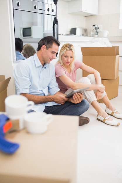 Couple using digital tablet amid boxes in house