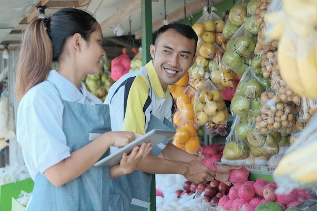 Coppia utilizzando la tavoletta digitale mentre si sceglie la mela quando si prepara un display del negozio di frutta