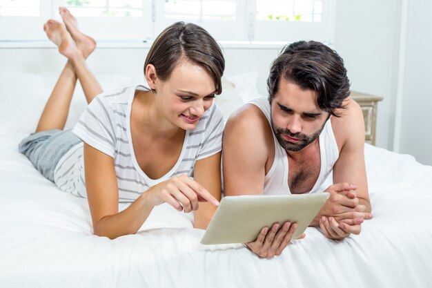 Couple using digital tablet while lying on bed