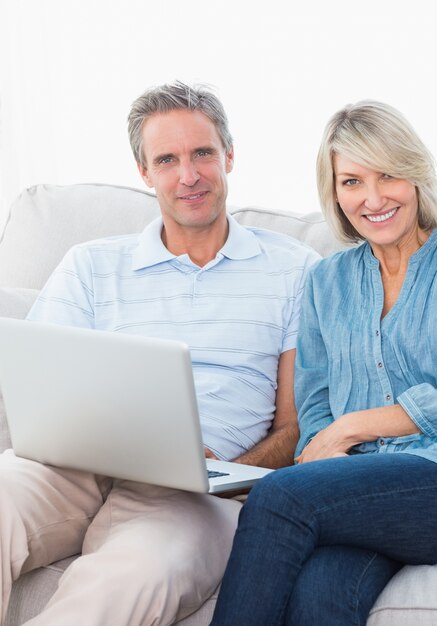 Couple using laptop together on the couch smiling at camera