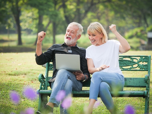 사진 공원 의 벤치 에 앉아 있는 커플 이 노트북 을 사용 하고 있다