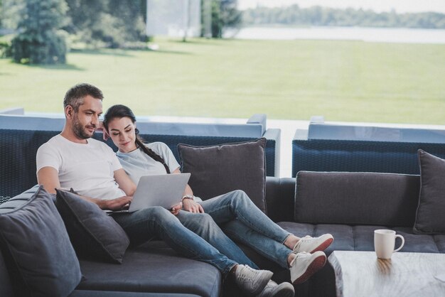 Couple using laptop while sitting on sofa at home