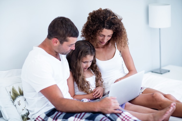 Couple using laptop with their daughter on bed