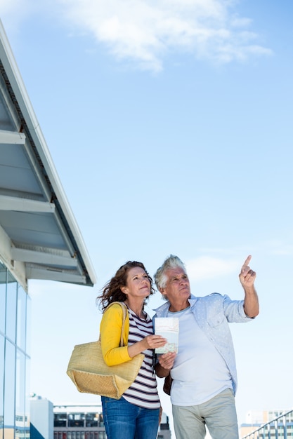 Couple using map against sky in city