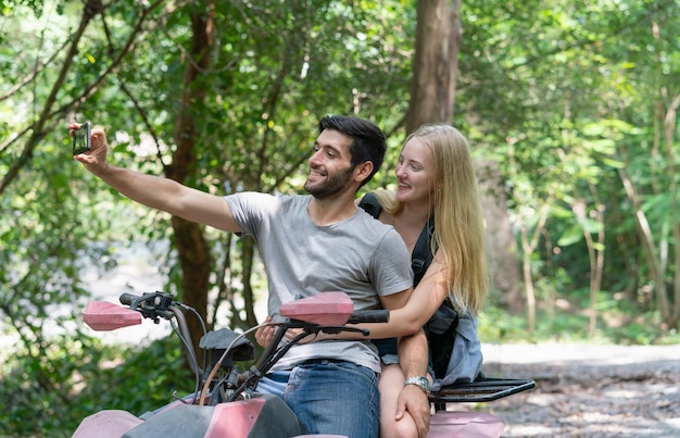 Пара, использующая селфи-фото камеры смартфона во время езды по бездорожью или на квадроцикле по дороге в лесу