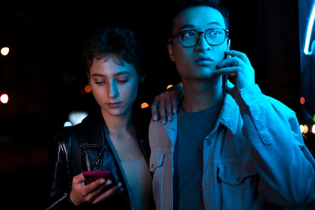 Photo couple using smartphones at night time in blue neon light