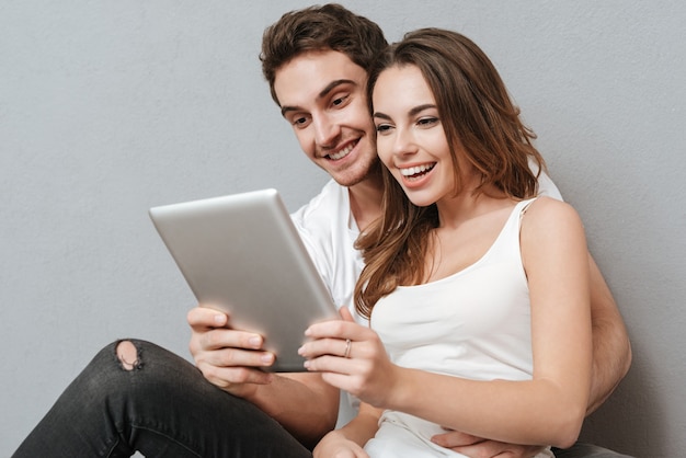 Couple using tablet computer on the floor . Isolated gray wall