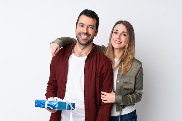 Couple in Valentine Day holding a gift over isolated wall hugging