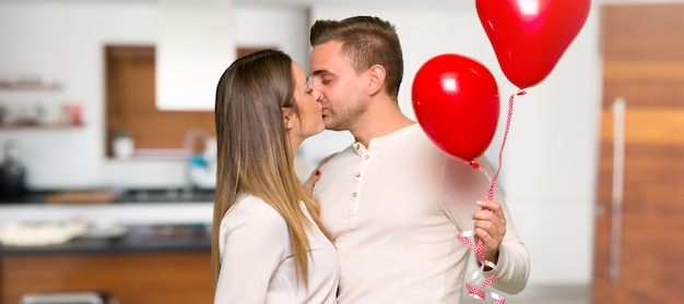 Couple in valentine day holding a heart symbol and balloons in a house