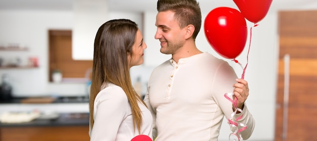 Couple in valentine day holding a heart symbol and balloons in a house