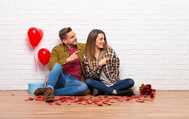 Couple in valentine day at indoors pointing finger to the side