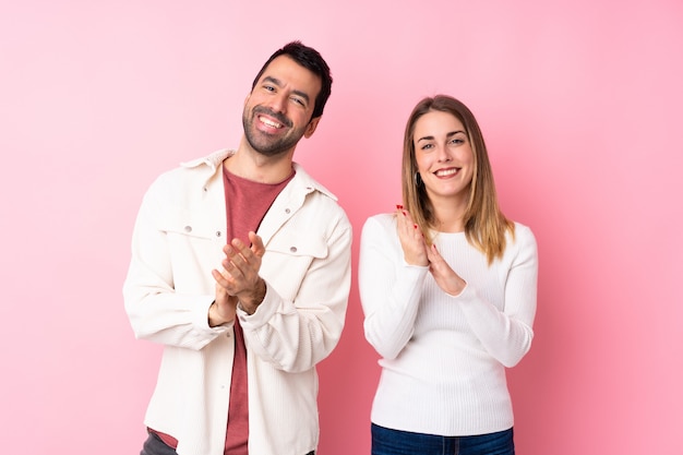 Couple in valentine day over isolated pink wall applauding after presentation in a conference