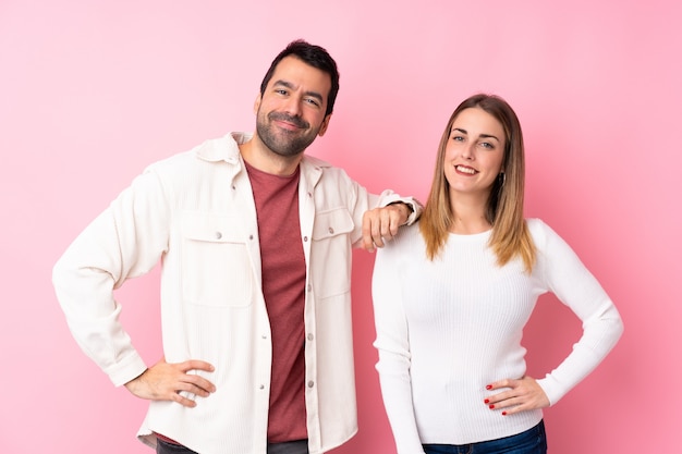 Coppie nel giorno di s. valentino sopra la parete rosa isolata che posa con le armi all'anca e a sorridere