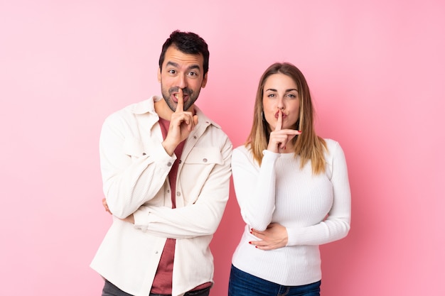 Couple in Valentine Day over isolated pink wall showing a sign of silence gesture putting finger in mouth