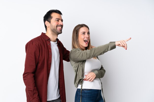 Couple in Valentine Day over isolated wall pointing finger to the side and presenting a product