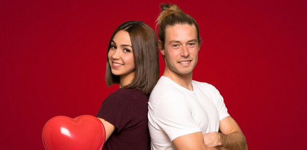 Couple in valentine day keeping the arms crossed looking at each other over red background