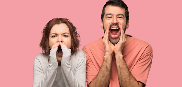 Couple in valentine day shouting and announcing something over isolated pink background