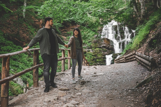 Couple walk holding hands waterfall on background