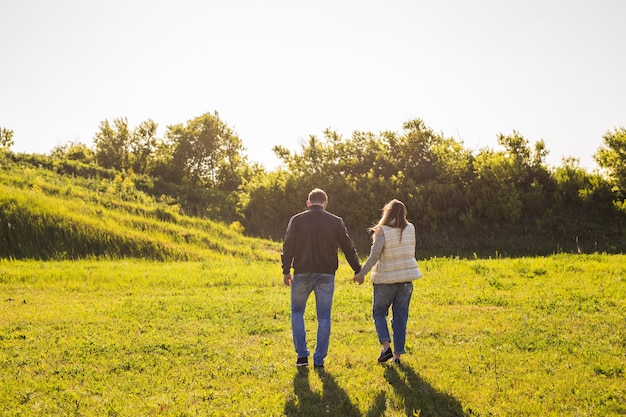 Couple walking in autumn sunset countryside meadow holding hands.